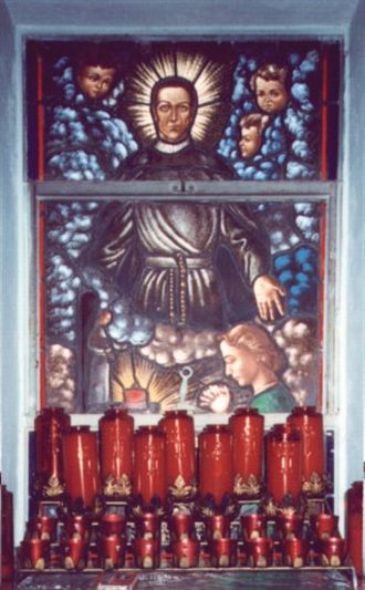 A painting of jesus is on the wall above candles.