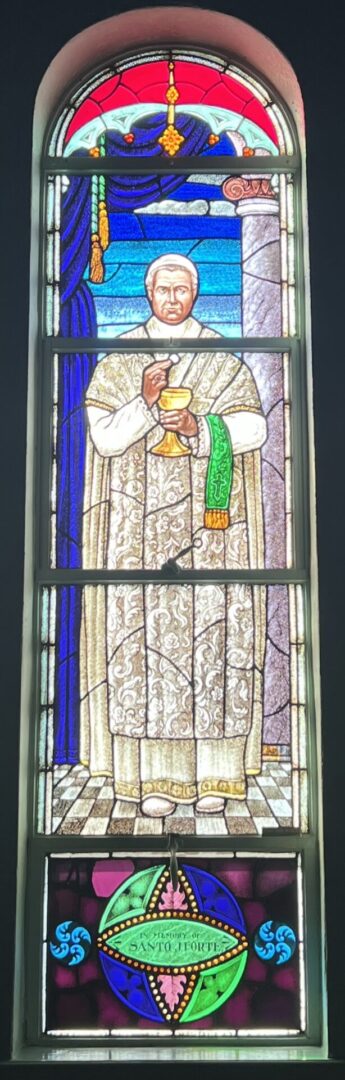 A stained glass window of a priest holding a cup.
