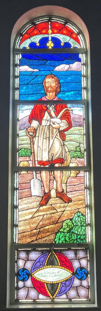 A stained glass window of a shepherd holding a shovel.